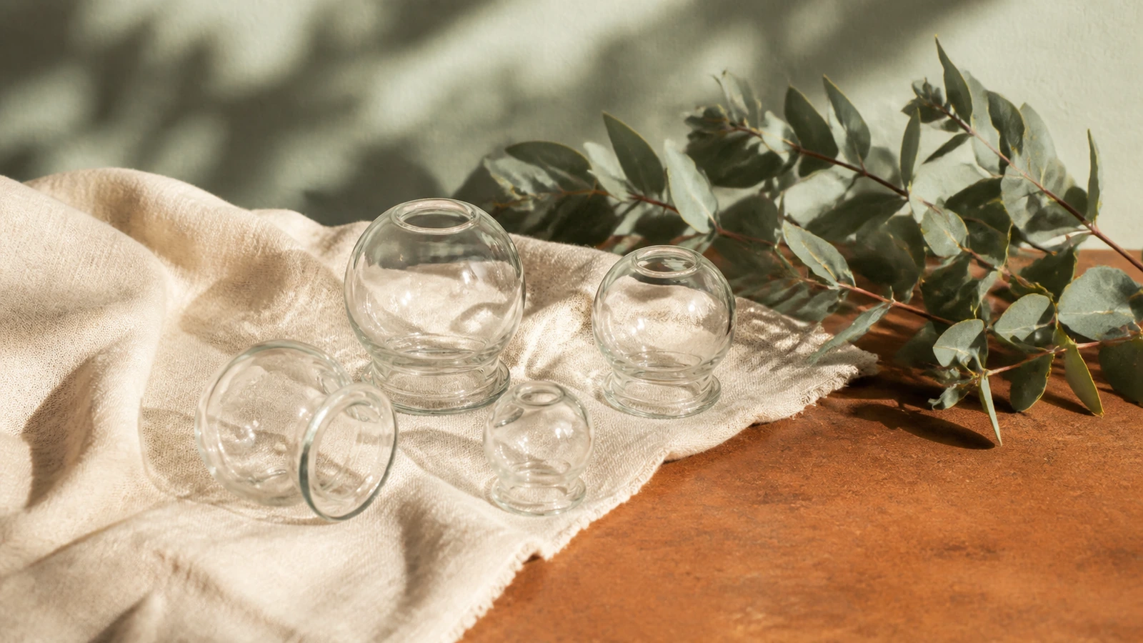 glazen cups op linnen naast eucalyptustak, stilleven
