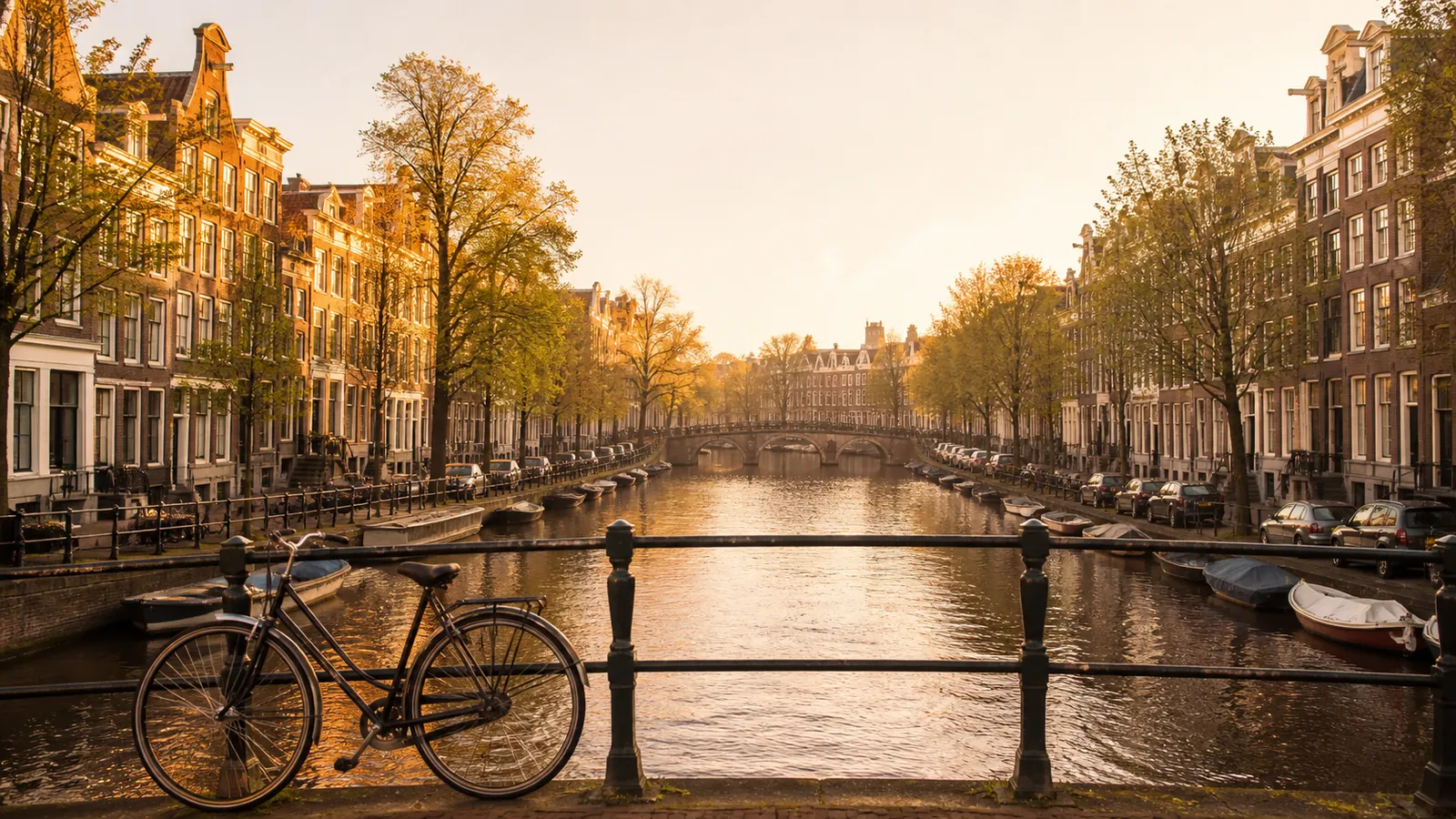 herkenbaar stadsbeeld van amsterdam: grachtenpand-gevels met ochtendlicht en een fiets tegen een brugleuning; warme editorial-stijl, geen close-ups van personen
